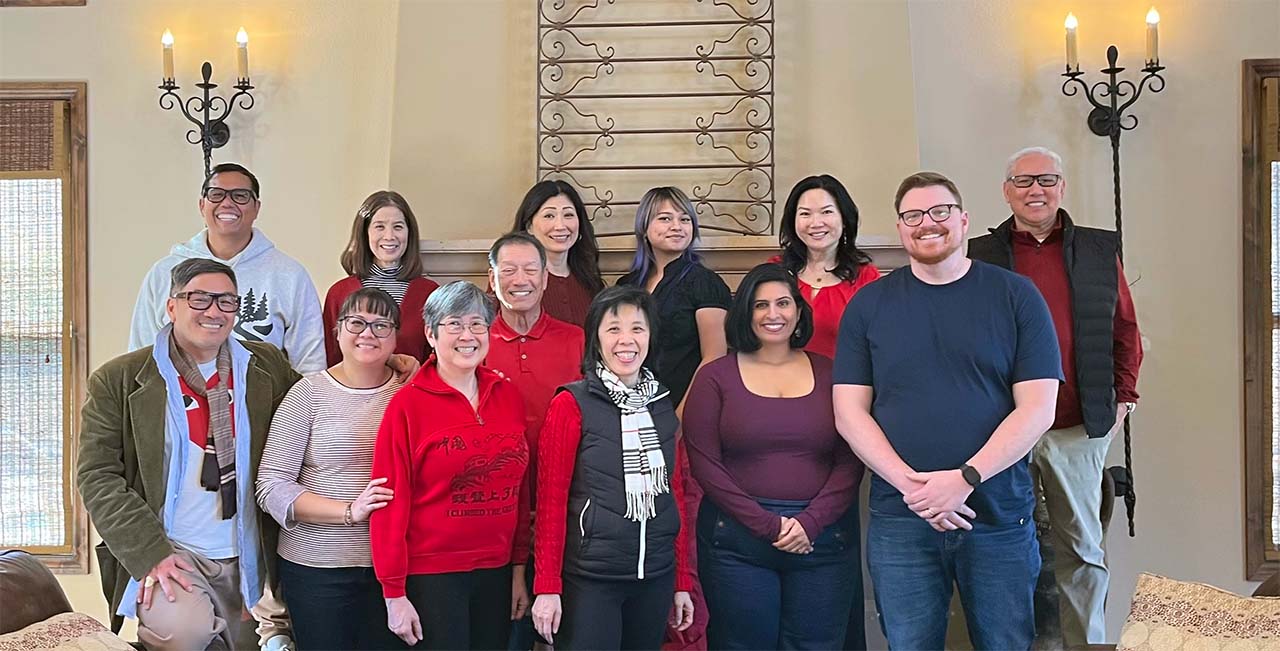Group of people pose for a photo in a living room, with two large light fixtures in the background.